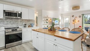A modern kitchen with white cabinetry, a wooden island, stainless steel appliances, and a view of the outdoors. - Newly Remodeled Lush Boho Vibe (Apollo Beach)