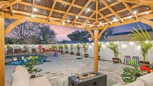 A covered outdoor area with a pool, seating, and a fire pit. - Newly Remodeled Lush Boho Vibe (Apollo Beach)