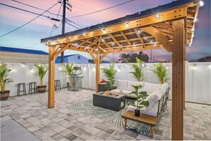 A covered outdoor patio with a grill, seating area, and string lights. - Newly Remodeled Lush Boho Vibe (Apollo Beach)