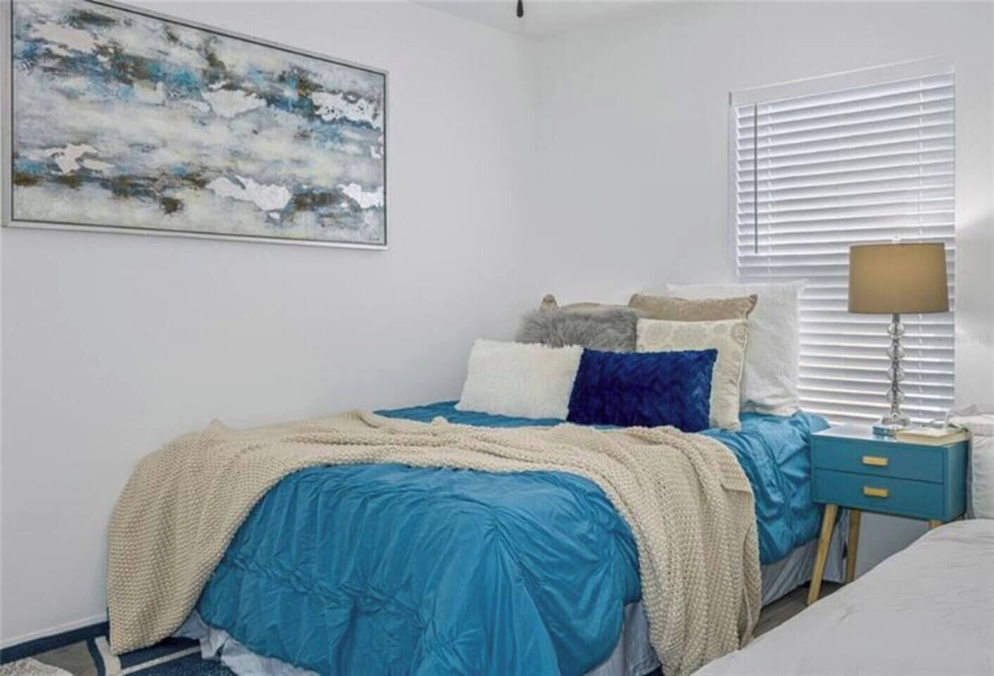 Une chambre à coucher avec un lit, une table de chevet, une lampe et une fenêtre avec des stores.