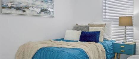 Une chambre à coucher avec un lit, une table de chevet, une lampe et une fenêtre avec des stores.