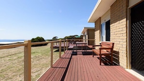 A wooden deck with benches overlooking a beach, a brick building with a window, and a fence.