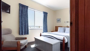 A bedroom with a bed, a chair, a window with curtains, and a television on the wall.