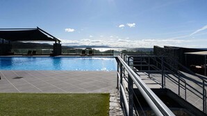 A rooftop pool with a clear view of the mountains, a covered seating area, and a stone wall.