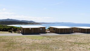 A row of two-story cabins with a view of the ocean and hills in the background.