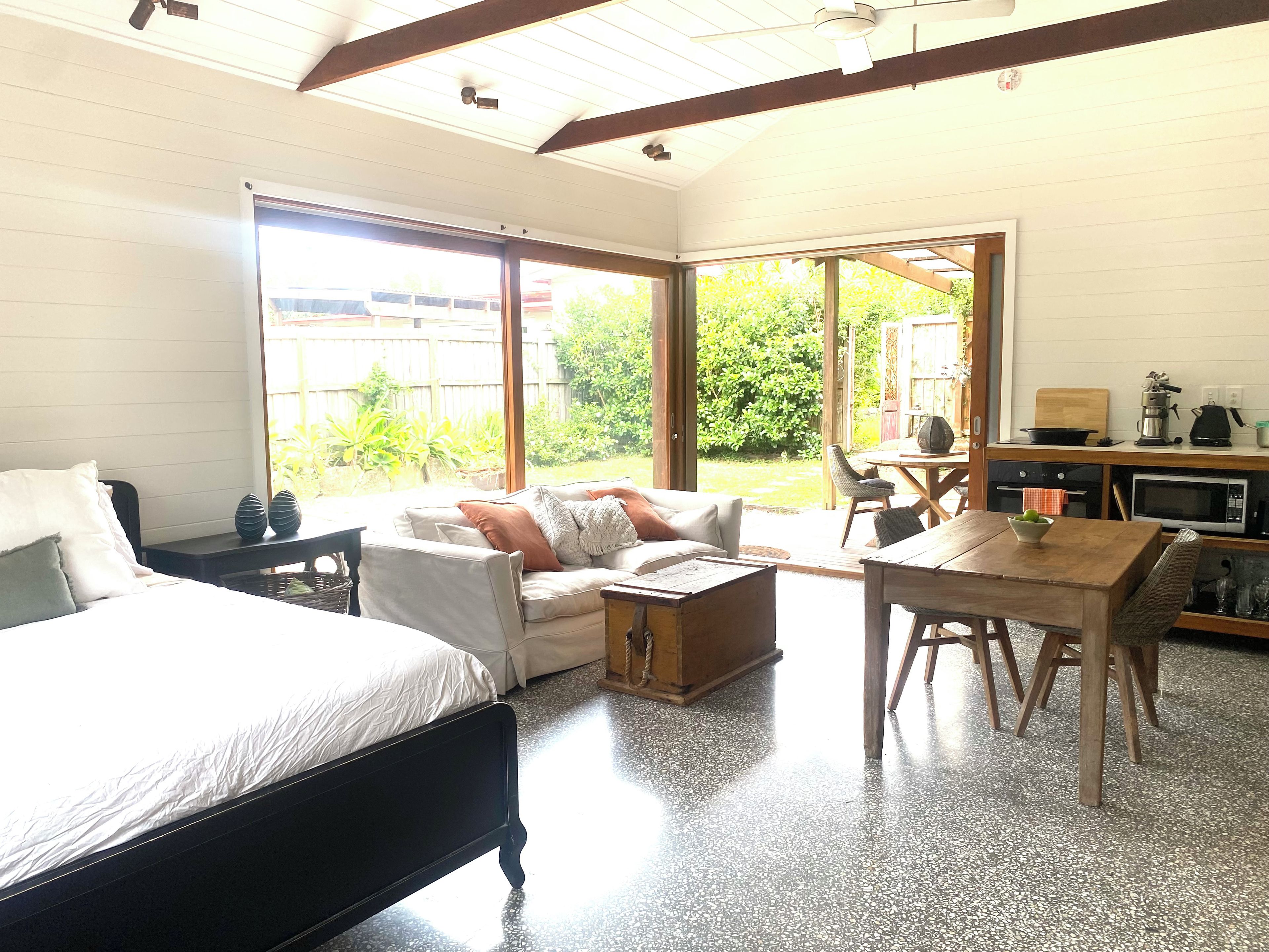 A bedroom with a bed, a sofa, a dining table, and a kitchen area with a microwave.