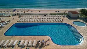 Área de piscina com espreguiçadeiras e vista para a praia e oceano.