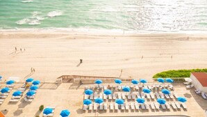 Um hotel à beira-mar com fileiras de espreguiçadeiras e guarda-sóis, área de piscina e vista para o oceano.