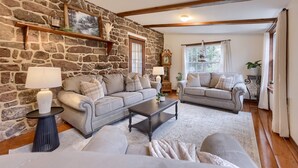 A cozy living room with stone walls, two sofas, a coffee table, and a fireplace. - Cedar Glen Farmhouse • 1800s Stone Retreat (Mohnton)