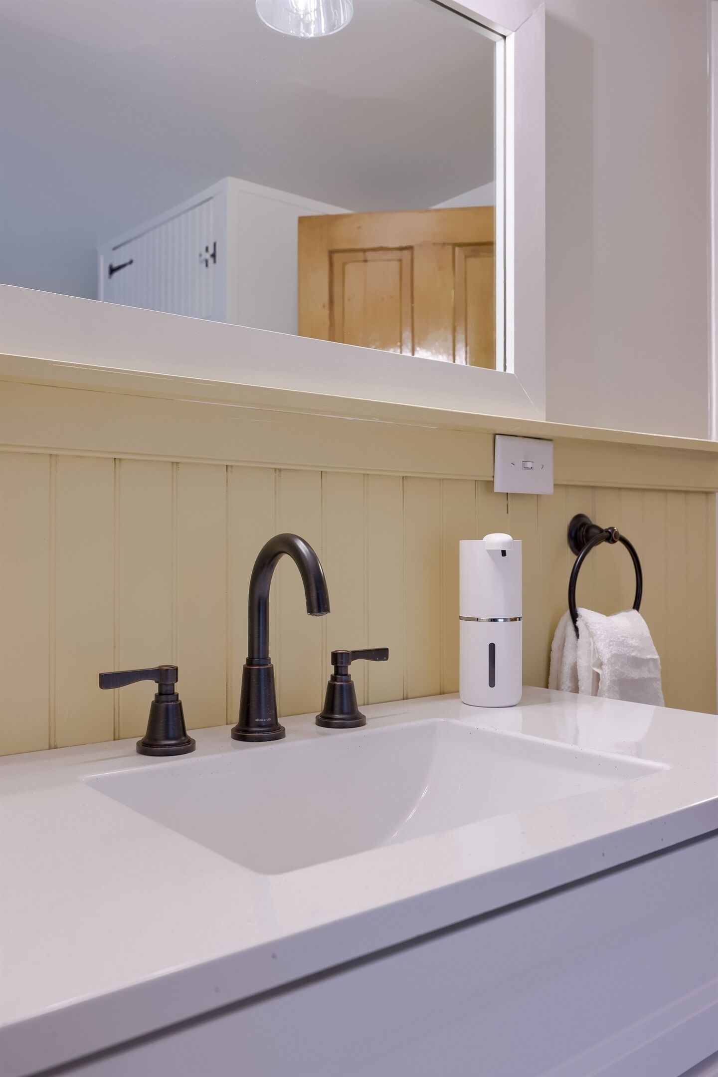 A bathroom with a white sink, two black faucets, a white soap dispenser, and a towel ring.