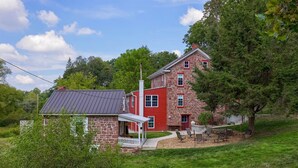 A two-story stone house with a red exterior and a small attached structure. - Cedar Glen Farmhouse • 1800s Stone Retreat (Mohnton)