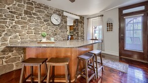 A kitchen with a stone wall, wooden bar stools, a clock, and a ceiling fan. - Cedar Glen Farmhouse • 1800s Stone Retreat (Mohnton)