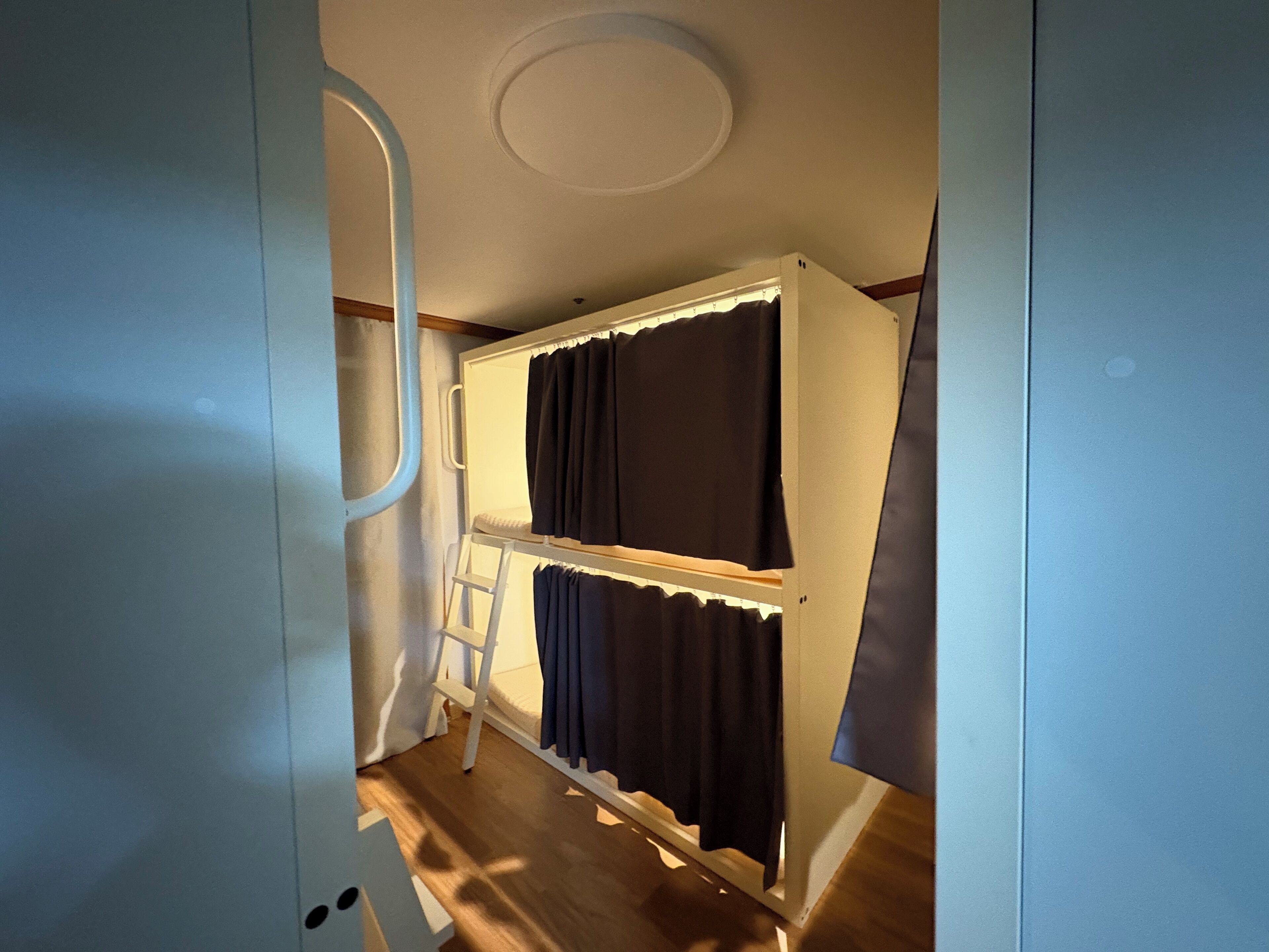 A compact room with bunk beds, a ladder, and a ceiling light fixture.