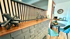 Une cuisine avec un mur de fond en briques, un plan de travail en bois et un coin repas comprenant une table ronde et des chaises bleues.