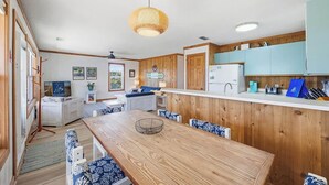 Een compacte keuken met houten kastjes, een eettafel met blauwe, geruite stoelen en een hanglamp.