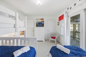 Ein Schlafzimmer mit zwei Betten, einer weißen Kommode, einem Stuhl und einer Tür, die auf einen Balkon führt.