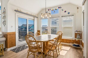 Uma sala de jantar com mesa redonda e cadeiras, janelas amplas e vista para edifícios.