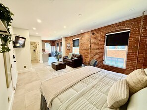 A modern bedroom with a large bed, a TV, and a brick wall. - Modern Rustic Luxury - Studio (Moncton)