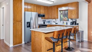Una cocina moderna con armarios de madera, una isla central con taburetes de bar, electrodomésticos de acero inoxidable y una ventana con vistas.