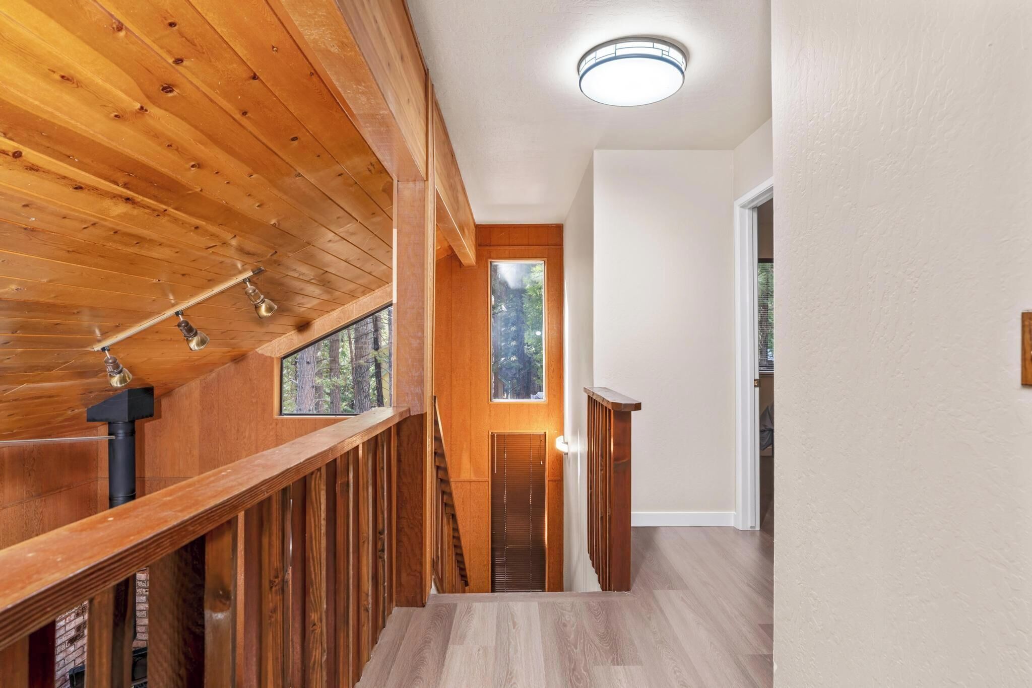 Un interior de madera con una escalera, una puerta con vistas y una lámpara en el techo.