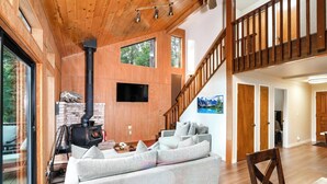 Una sala de estar moderna con chimenea de piedra, un sofá seccional grande y una escalera de madera.