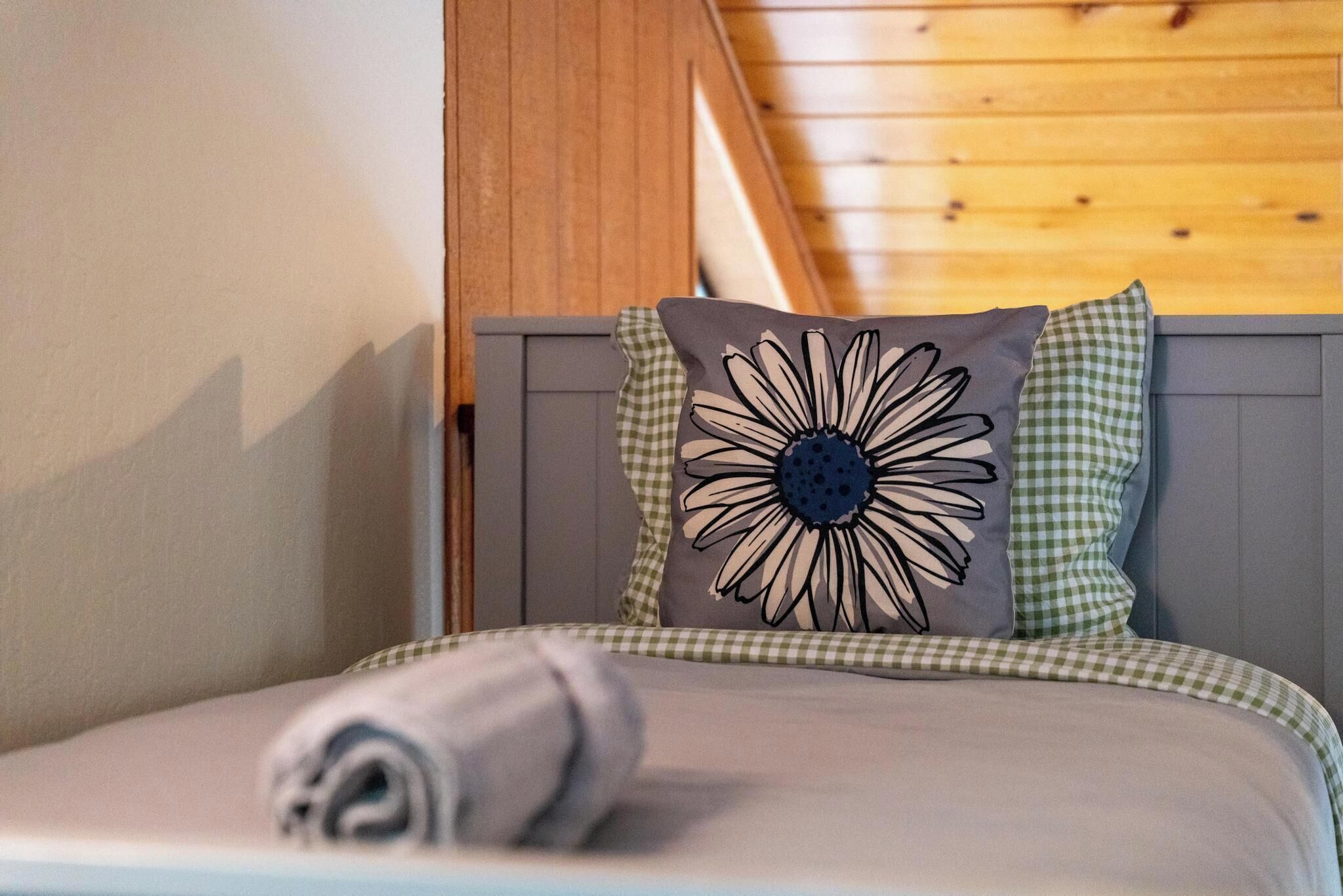 Un lit avec un oreiller orné d’un grand motif floral, des coussins à carreaux et une serviette enroulée.