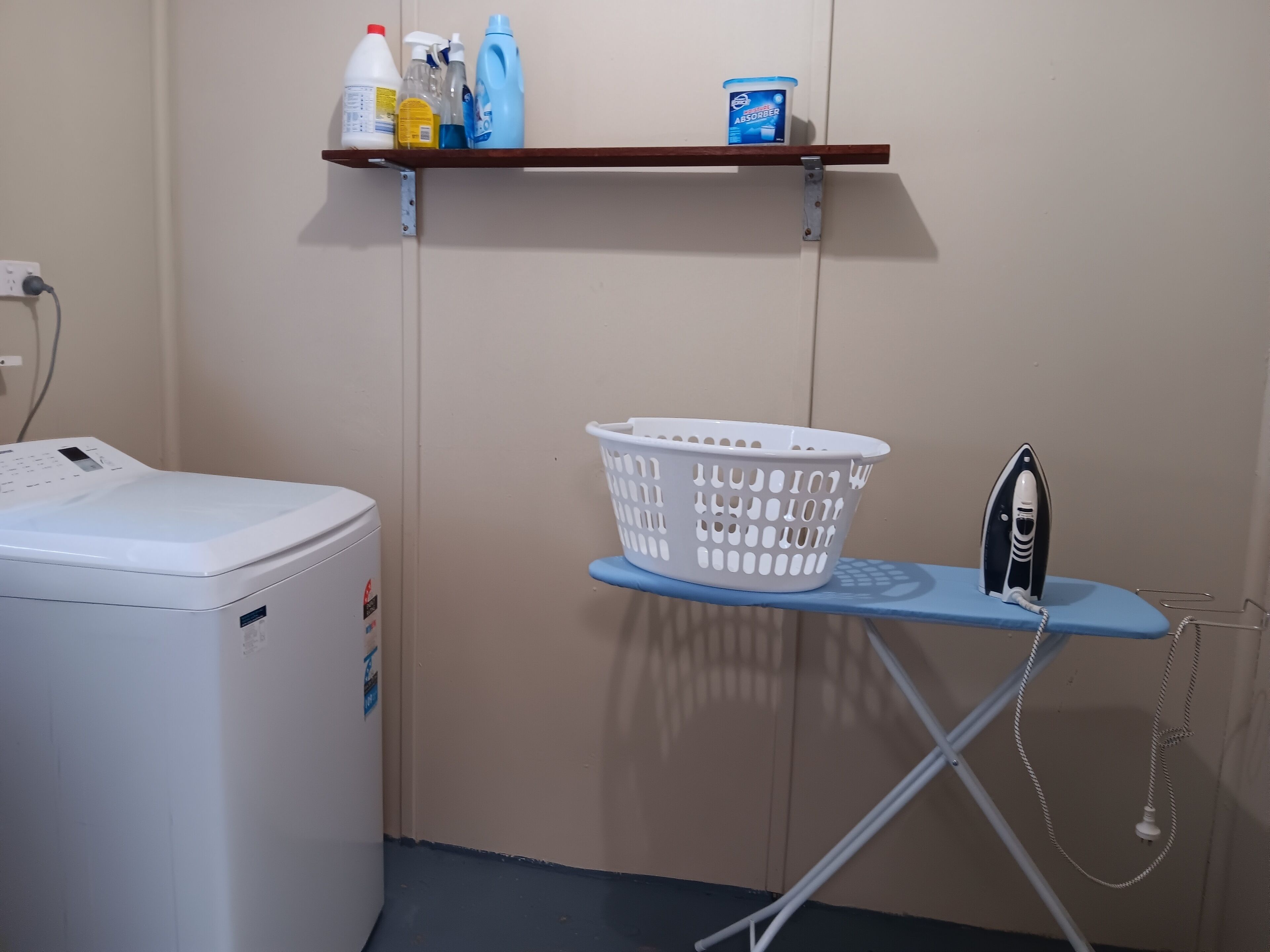 A laundry area with a washing machine, a drying rack, a shelf with cleaning supplies, and a laundry basket.