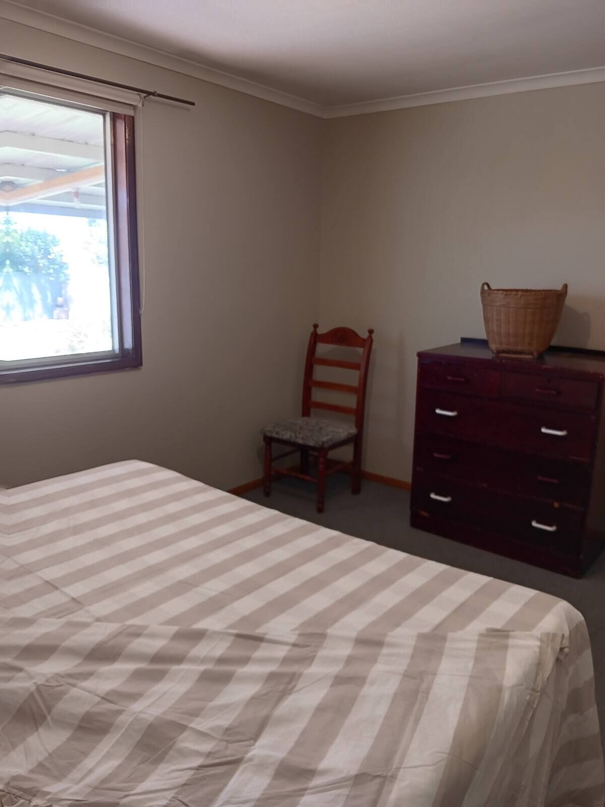 A bedroom with a bed, a chair, a dresser, and a window.