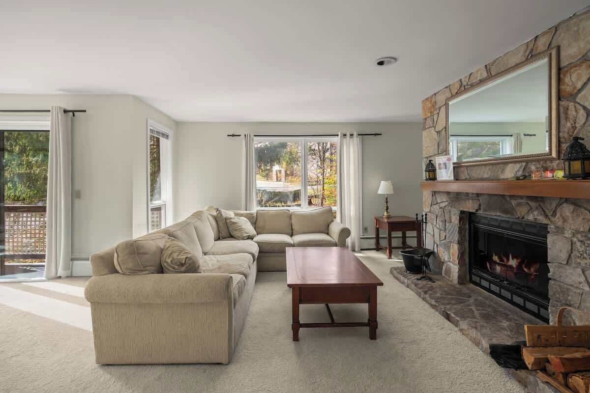 A living room with a stone fireplace, beige sofas, and a large window.