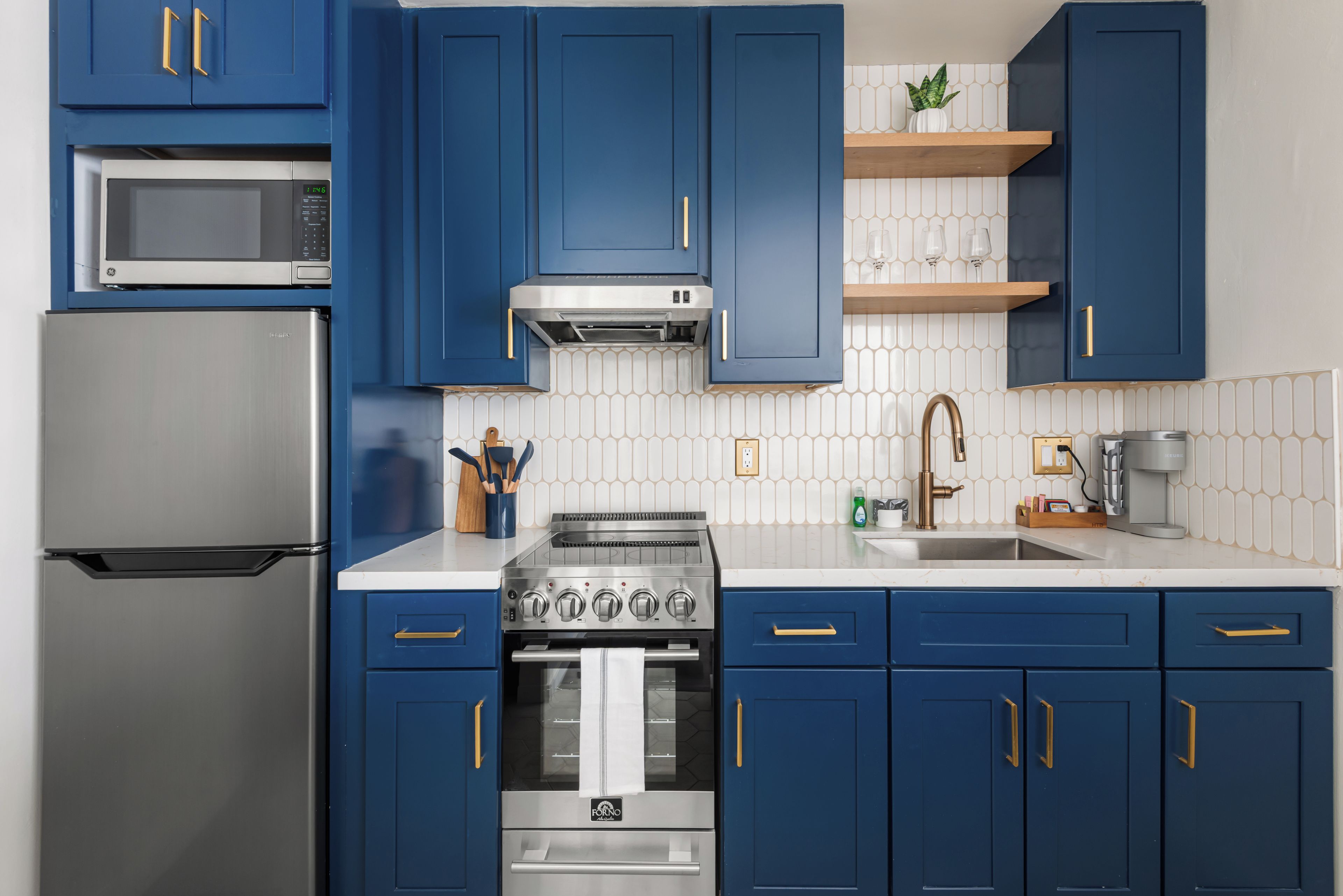 A modern kitchen with blue cabinets, stainless steel appliances, and a white tiled backsplash.