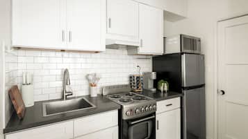 A modern kitchen with white cabinets, a stainless steel stove, and a black refrigerator.