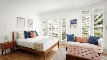 Une chambre à coucher comprenant un lit, une table de chevet et une commode. On y trouve une fenêtre avec des stores, un ventilateur de plafond et un téléphone fixé au mur.