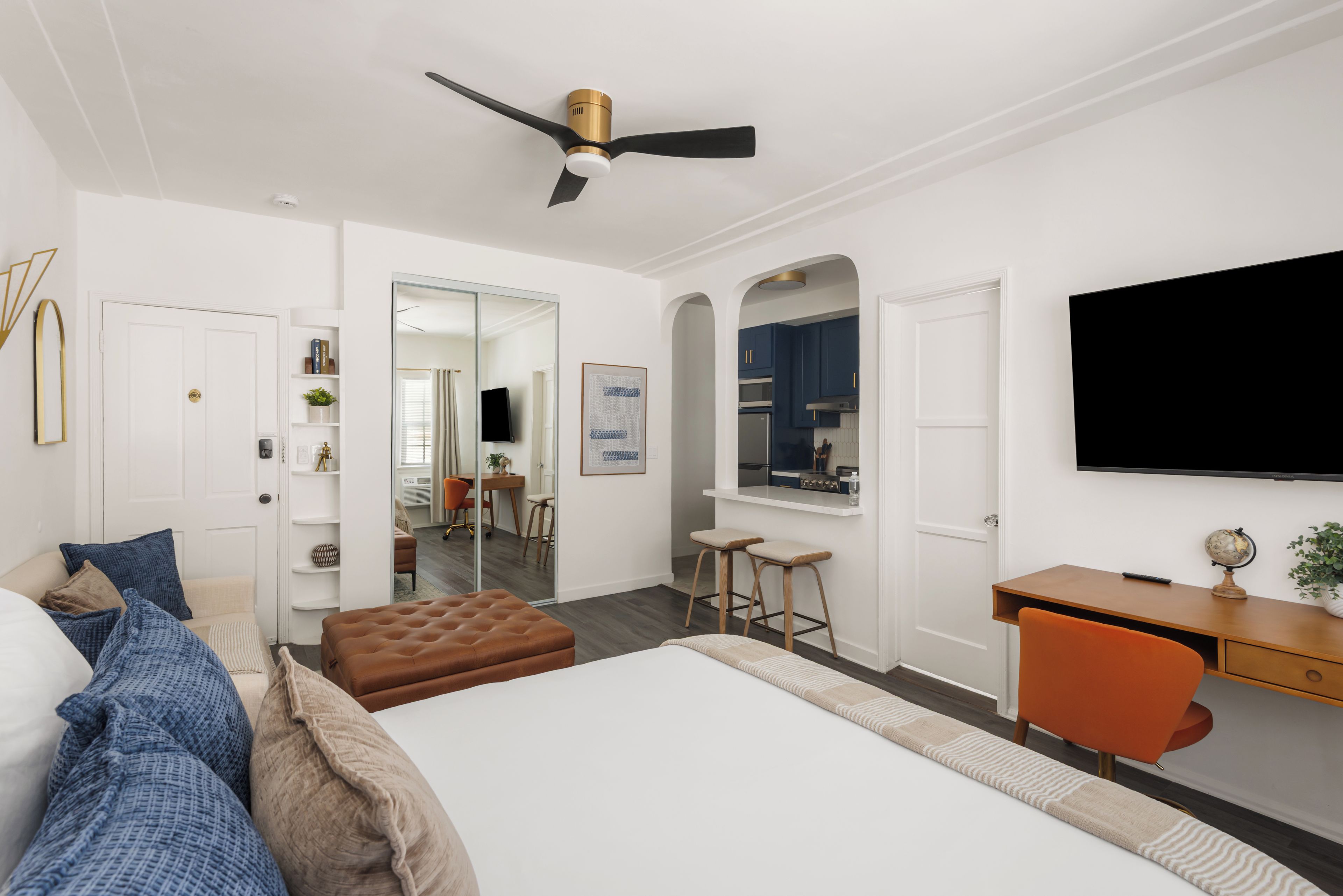 A modern bedroom with a bed, a desk, a TV, and a ceiling fan.