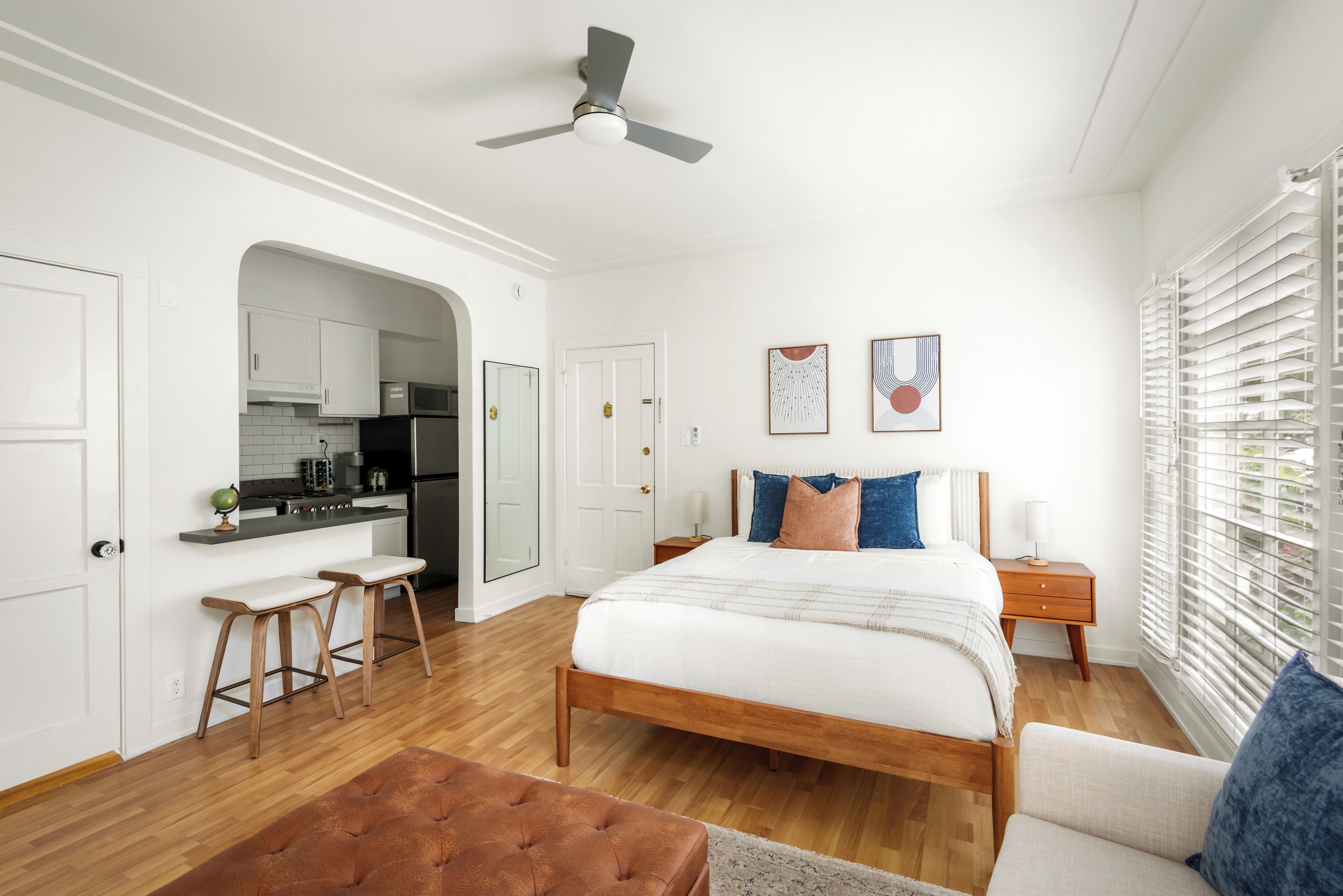 A bedroom with a bed, a nightstand, a chair, a bench, a ceiling fan, and a window with blinds.