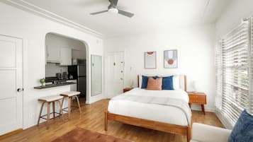 A bedroom with a bed, a nightstand, a chair, a bench, a ceiling fan, and a window with blinds.