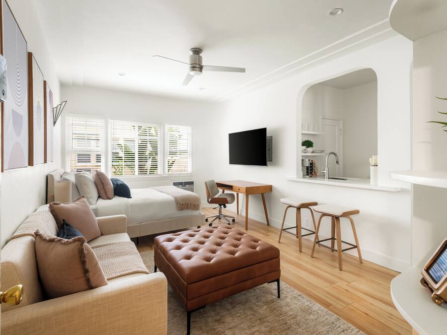 A modern living room with a sofa, ottoman, and a desk with stools.
