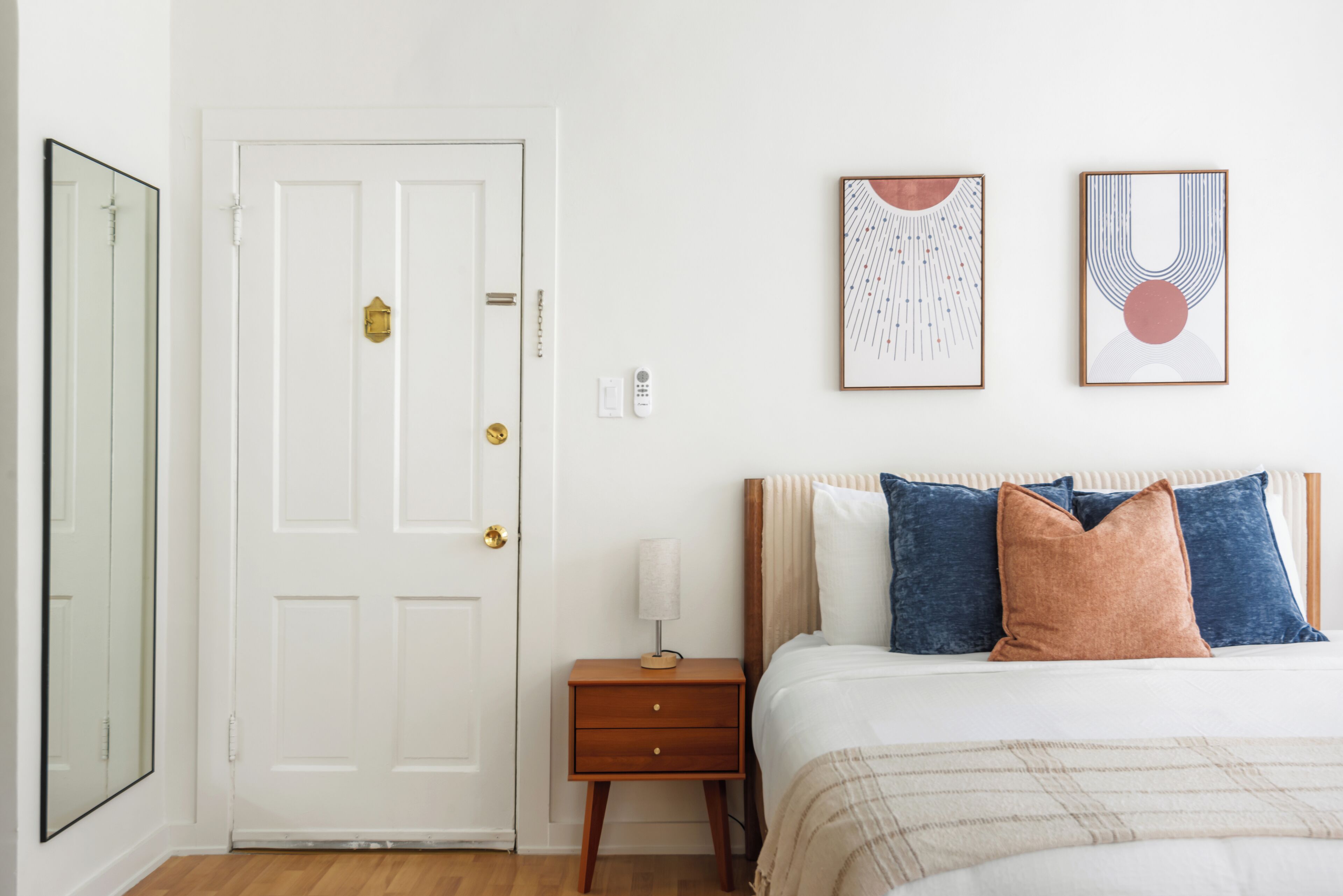 A bedroom with a bed, bedside table, lamp, and two framed artworks on the wall.