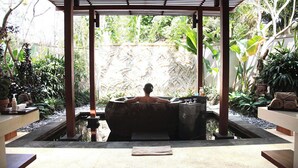 Eine Person entspannt sich in einer Hot Tub mit Blick auf einen üppigen Garten und eine Steinmauer.