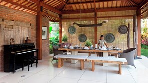 A covered outdoor dining area with a piano, a table set for dining, and decorative plates on the wall. - Dea Villas - Villa Sati by Elite Havens (Canggu)