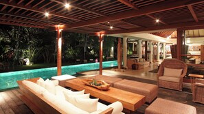 Ett område vid poolen med en träbänk, en soffa och en fåtölj i rotting.