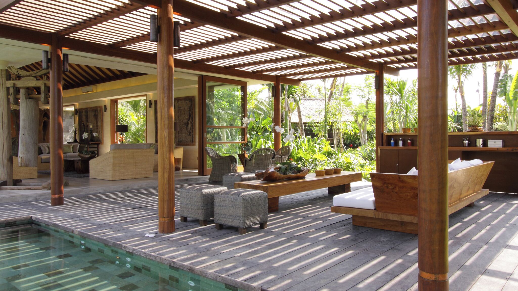 Un espace extérieur abrité, doté d’une piscine, de mobilier en bois et de plantes tropicales.