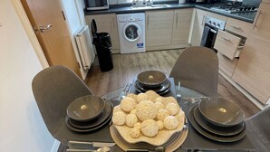 A modern kitchen with a dining table set for four, a washing machine, and a view of a building outside. - The Grounded Pearl (Salford)