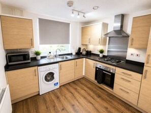 Une cuisine moderne avec des meubles en bois, une cuisinière en acier inoxydable, un lave-linge encastré et une fenêtre avec vue.