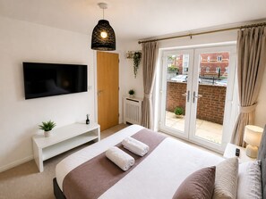 A bedroom with a bed, a TV, a sliding door to a balcony, and a white console table. - The Grounded Pearl (Salford)