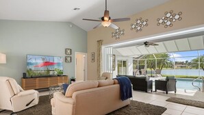 A spacious living room with a large sofa, a television, and a ceiling fan. There is a view of a pool and greenery outside. - Beautiful vacation home with great lake view and pool in Naples (Naples)