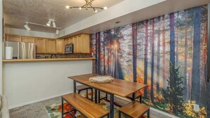 A modern kitchen with wooden cabinets, a stainless steel refrigerator, and a dining area with a bench and table.