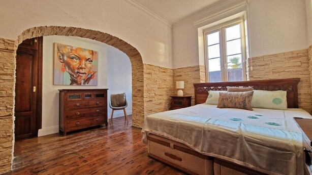 A bedroom with a stone wall, wooden furniture, a bed with multiple pillows, and a painting on the wall. - Private driveway + pool + views of the straits (Gibraltar)