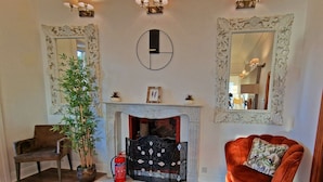A room with a fireplace, two wall-mounted lamps, a mirror, a potted plant, a chair, and a red velvet armchair. - Private driveway + pool + views of the straits (Gibraltar)