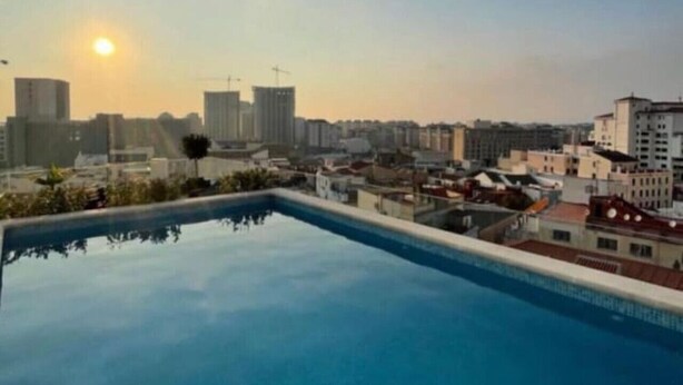 A rooftop pool with a cityscape view during sunset.