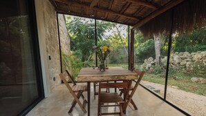 A wooden dining table with chairs, a vase with flowers, and a view of greenery through large windows. - Refugio en la Serva Maya Coba (Cobá)